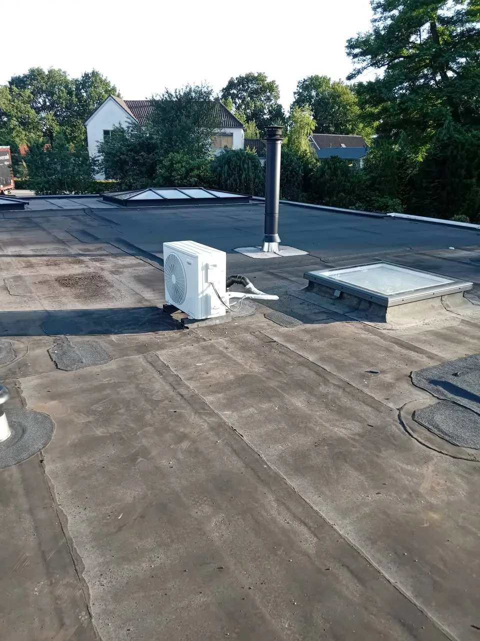 Airco buitenunit op een plat dak naast een lichtkoepel