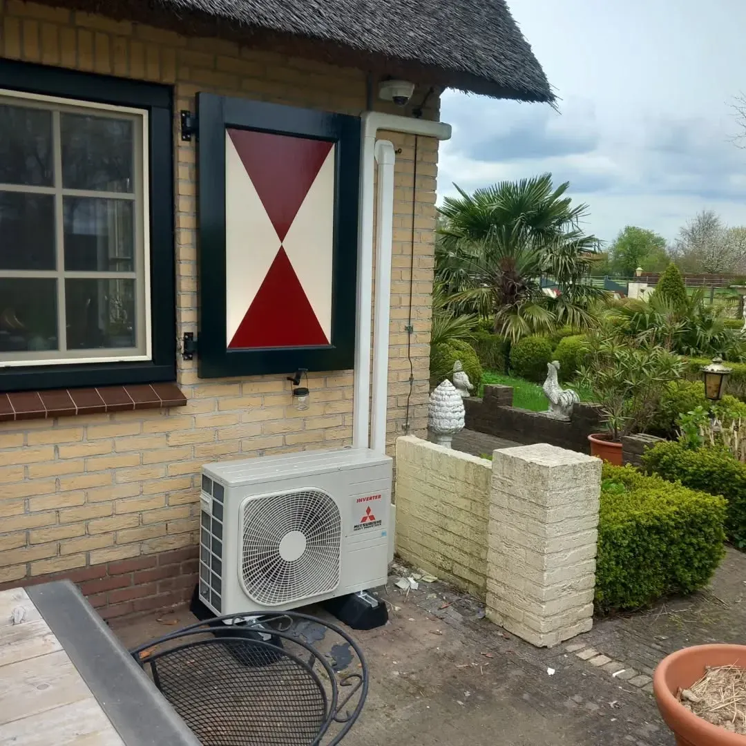 Buitenunit zorgvuldig geplaatst bij een woning met rieten dak